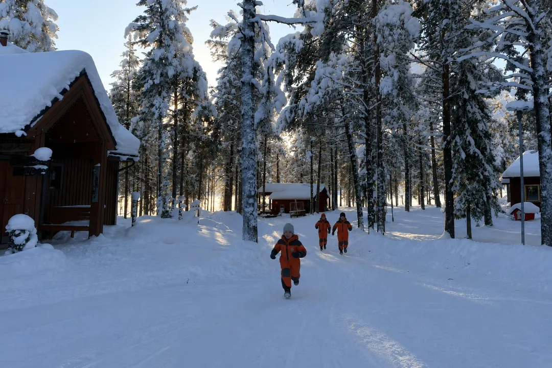 Children running through the snow between cabins at Torassieppi