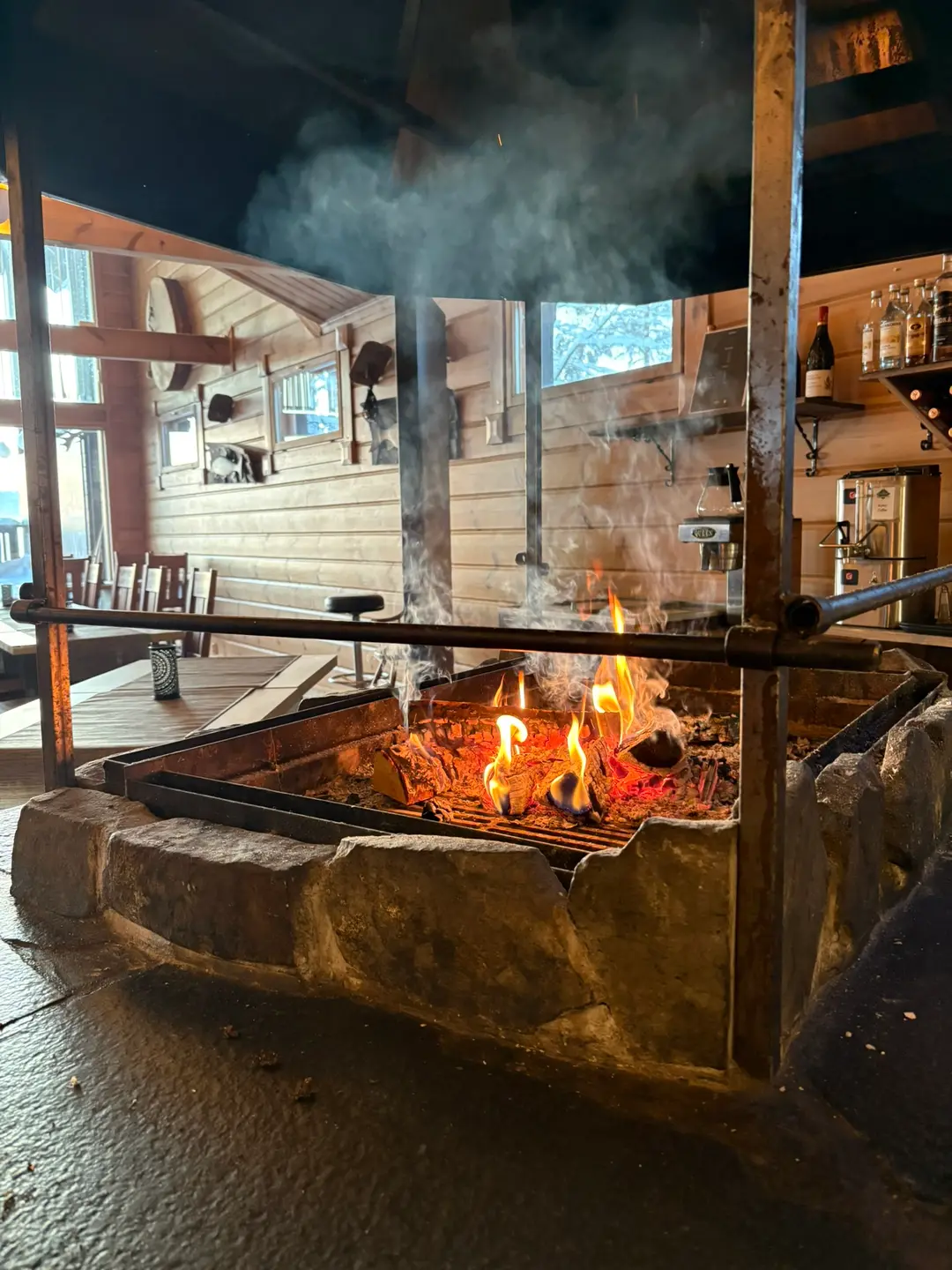 Large open stone fireplace with roaring log fire in a rustic wooden lodge