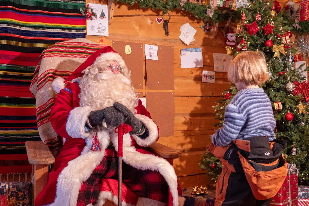Child meeting Santa in a cosy Christmas cabin beside a decorated tree