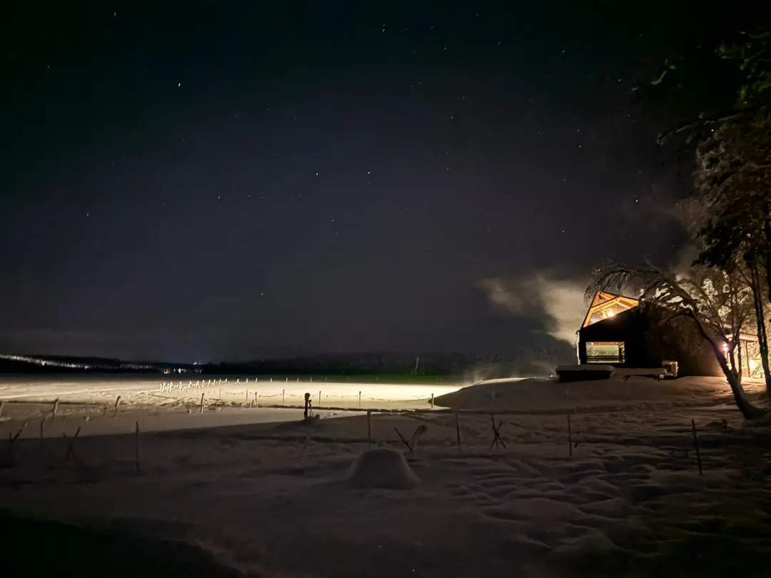 Glass-roofed sauna cabin on the edge of a frozen lake under a starry night sky